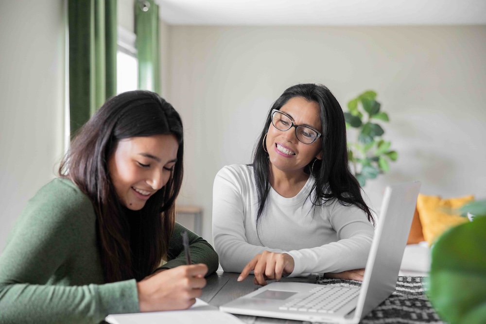 A woman is pointing and helping a young girl with her work.